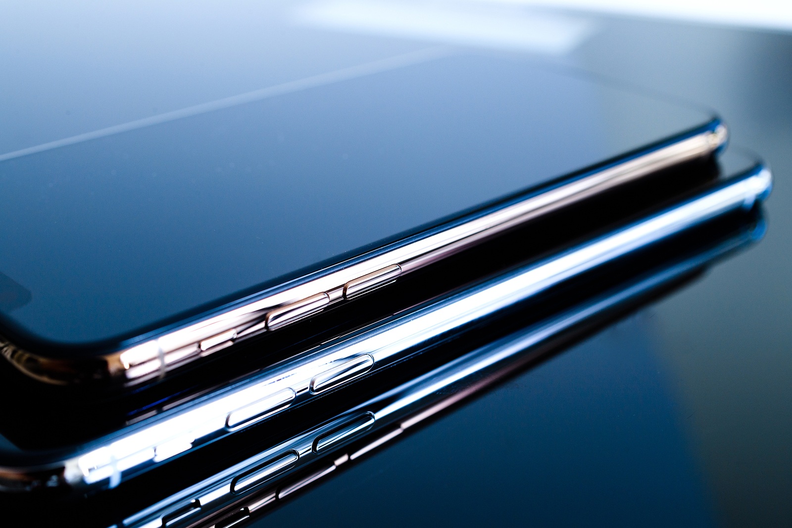 PARIS, FRANCE - SEP 25, 2018: One above another iPhone Xs and Xs Max smartphone model by Apple Computers close up of newest golden iPhone mobile phone device on technology blue reflective background