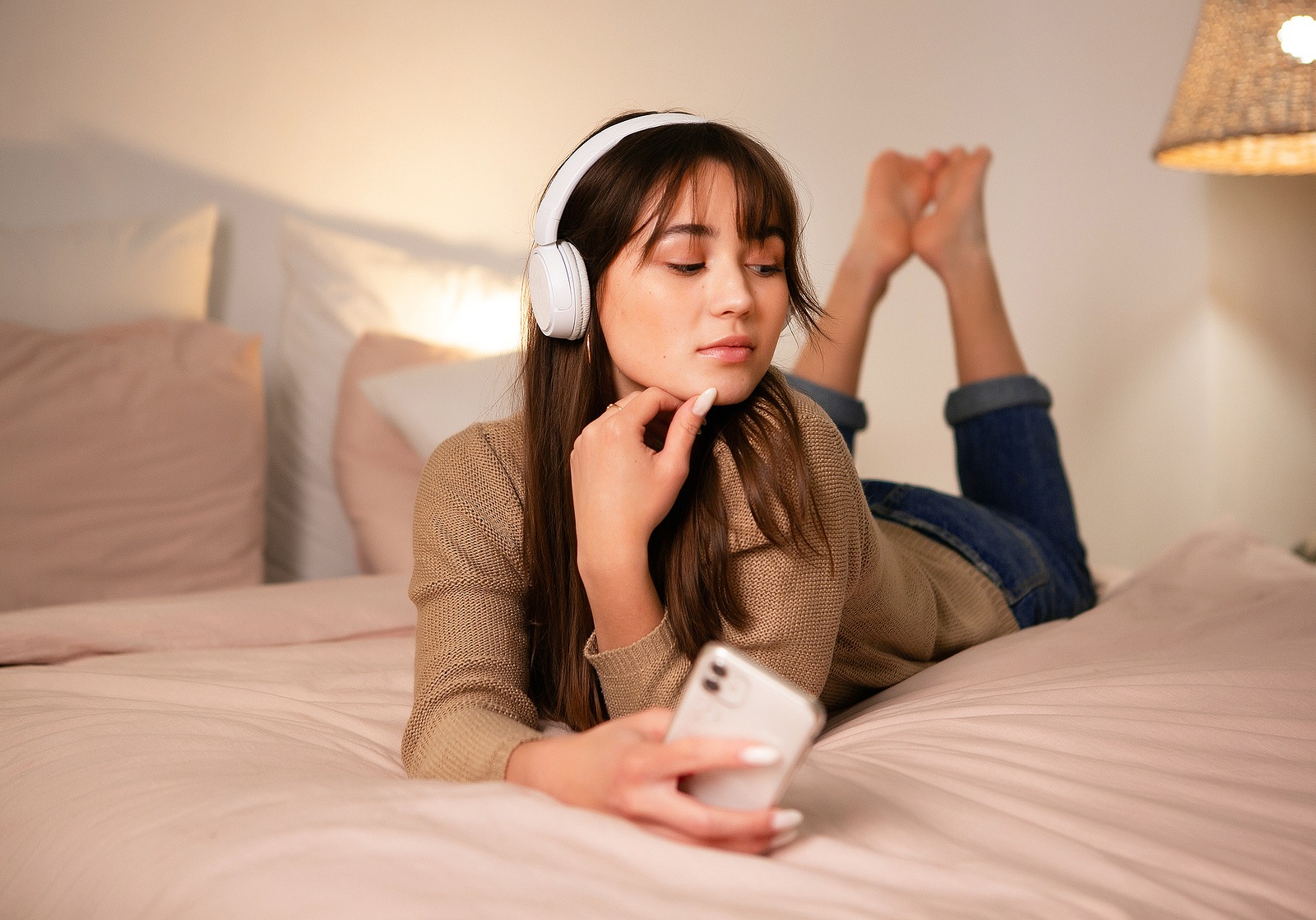 The girl lies on the bed with bluetooth headphones and a phone