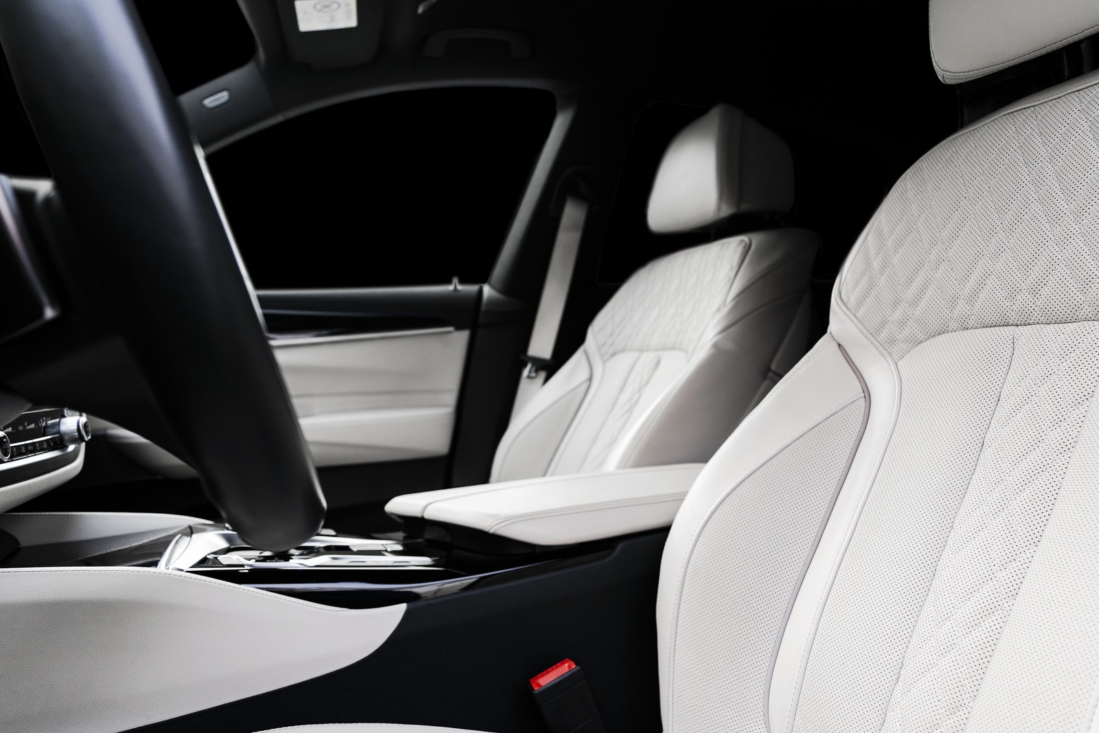 Modern luxury car white leather interior with natural wood panel. Part of leather car seat details with stitching. Interior of prestige modern car. White perforated leather. Car detailing. Car inside