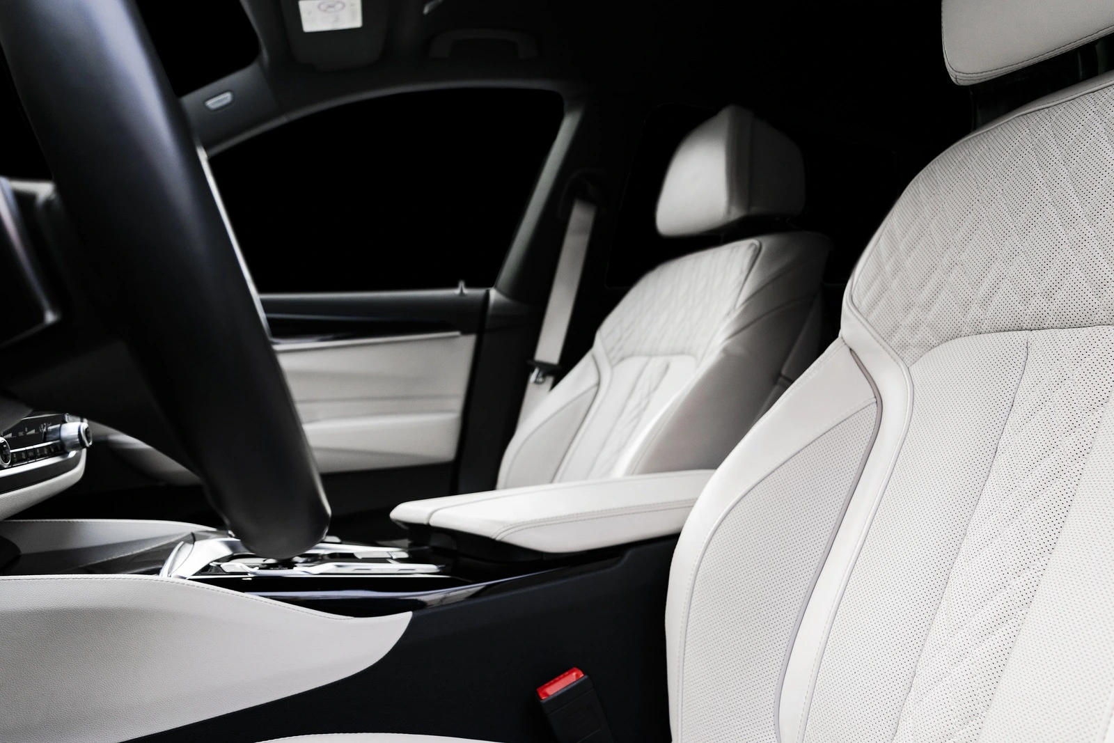 Modern luxury car white leather interior with natural wood panel. Part of leather car seat details with stitching. Interior of prestige modern car. White perforated leather. Car detailing. Car inside