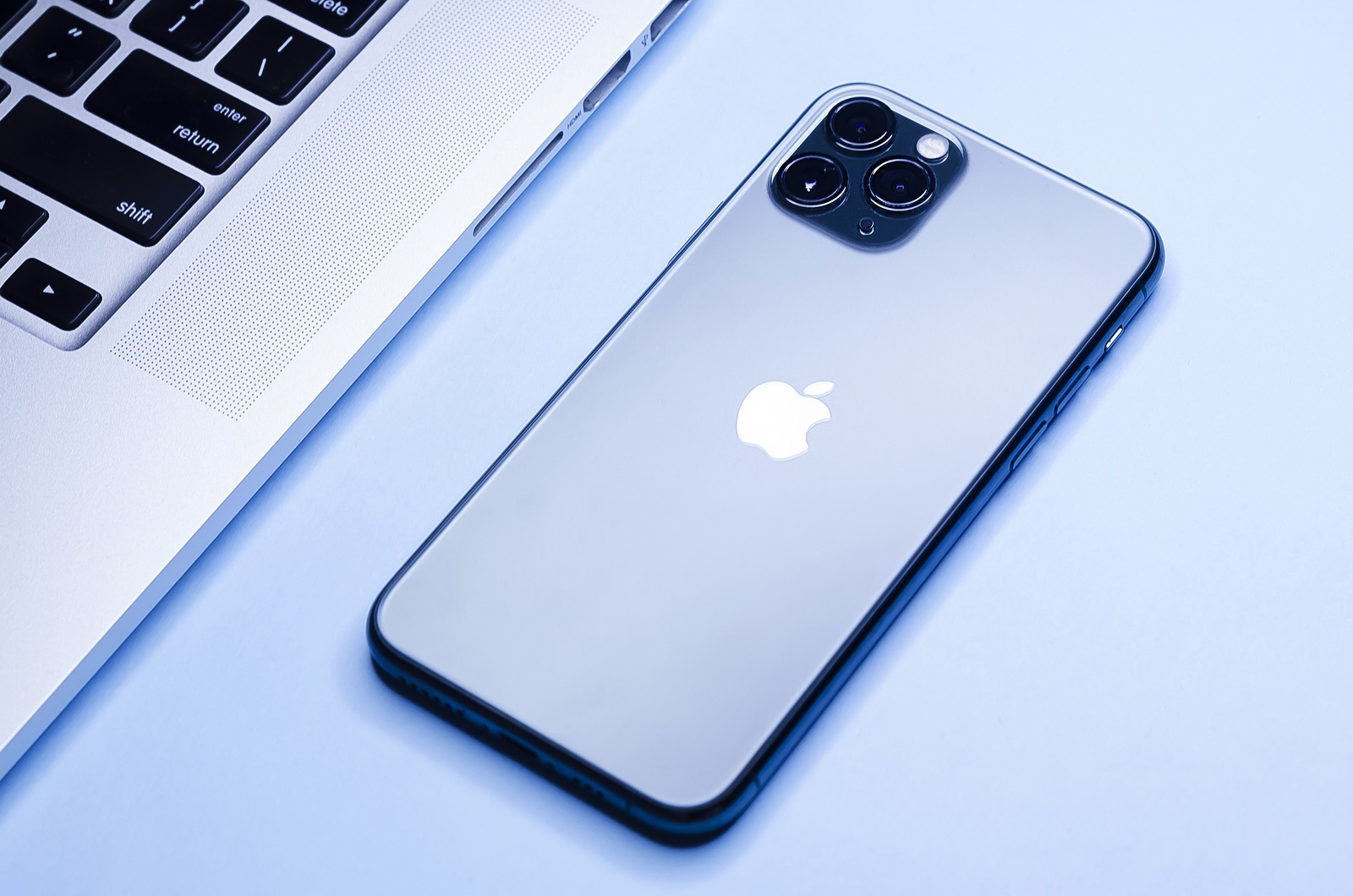 Russia, St. Petersburg, 01/12/2020: Apple technology, modern gadgets laptop Mac Pro, blue smartphone iPhone 11 with 3 three cameras on rear panel. soft focus