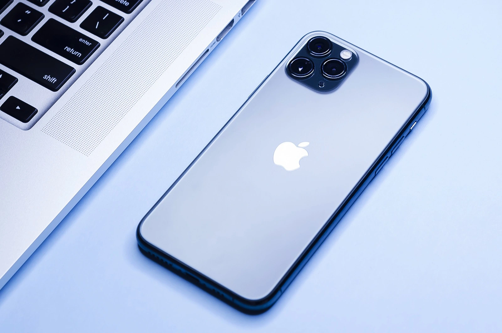 Russia, St. Petersburg, 01/12/2020: Apple technology, modern gadgets laptop Mac Pro, blue smartphone iPhone 11 with 3 three cameras on rear panel. soft focus