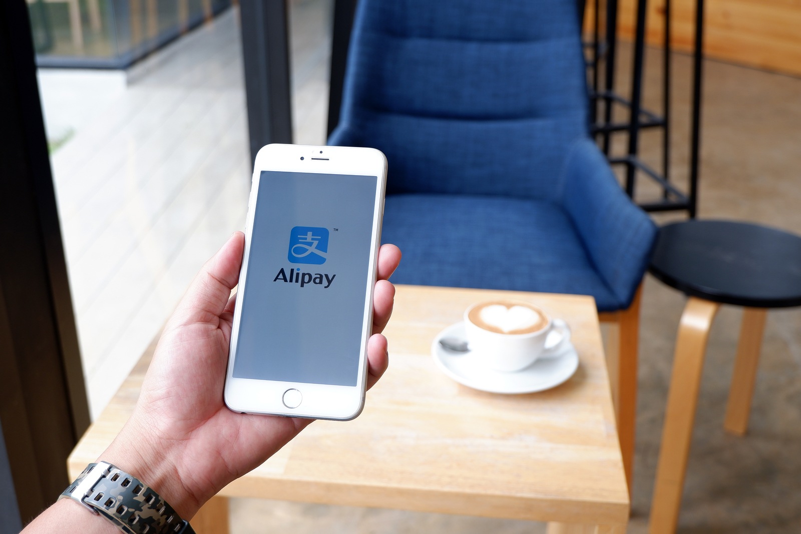 A man sit in cafe holding mobile with alipay screen