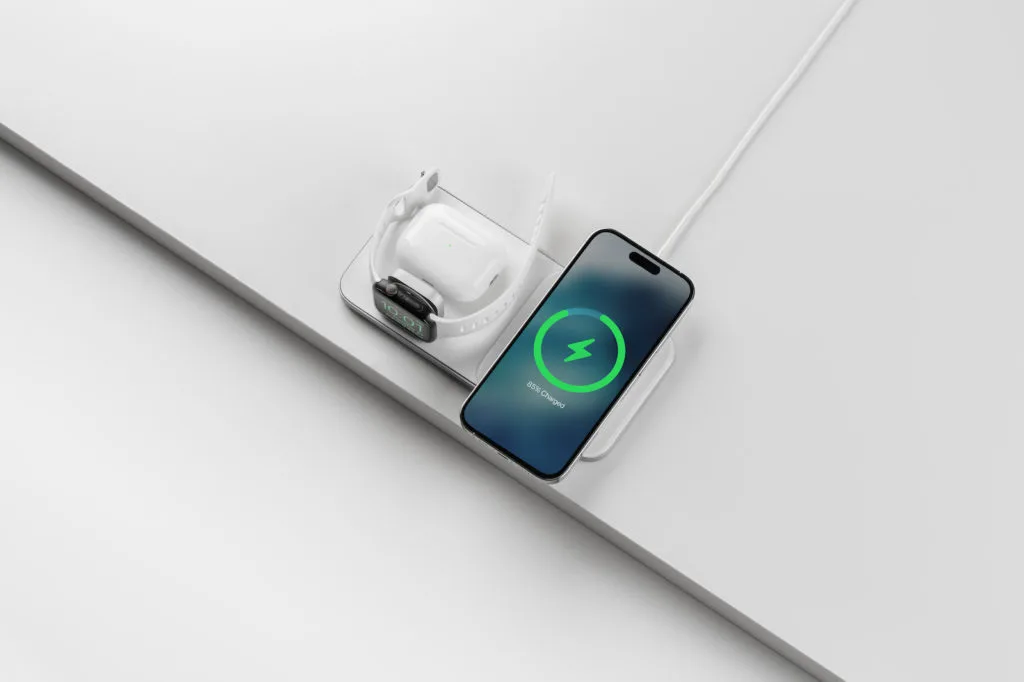 Das Nomad Base One Max 3-in-1 Ladegerät aus der Vogelperspektive beim gleichzeitigen Laden eines iPhones mit aktivem MagSafe-Ladebildschirm, AirPods und einer Apple Watch.