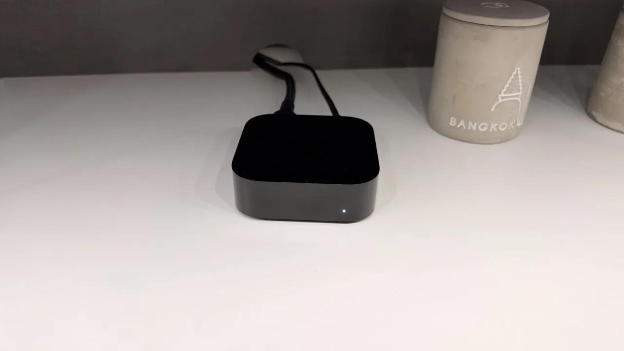 Apple TV oder Smart-TV: angeschlossenes Apple TV 4K mit leuchtender Statusanzeige und Kabeln auf einem weißen Regal