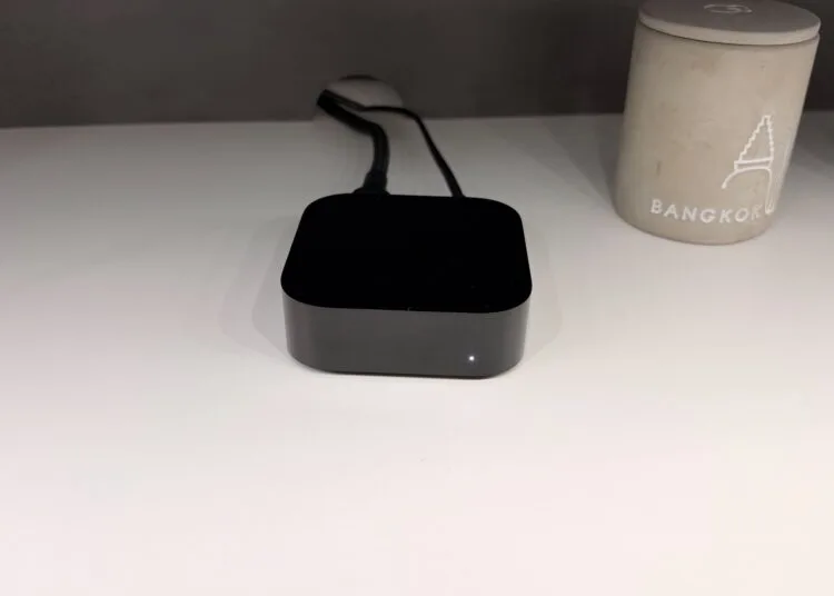 Apple TV oder Smart-TV: angeschlossenes Apple TV 4K mit leuchtender Statusanzeige und Kabeln auf einem weißen Regal