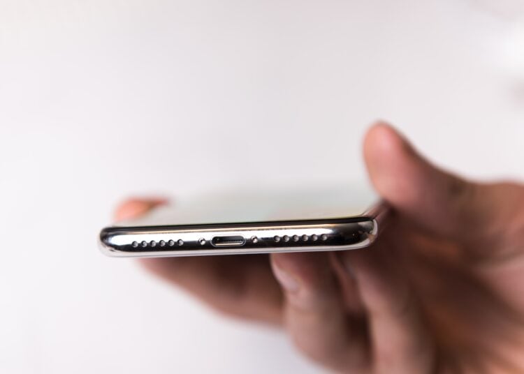 Symbolbild zum iPhone 20: iPhone in der Hand, Blick auf Unterseite mit Lautsprechergitter und Anschluss