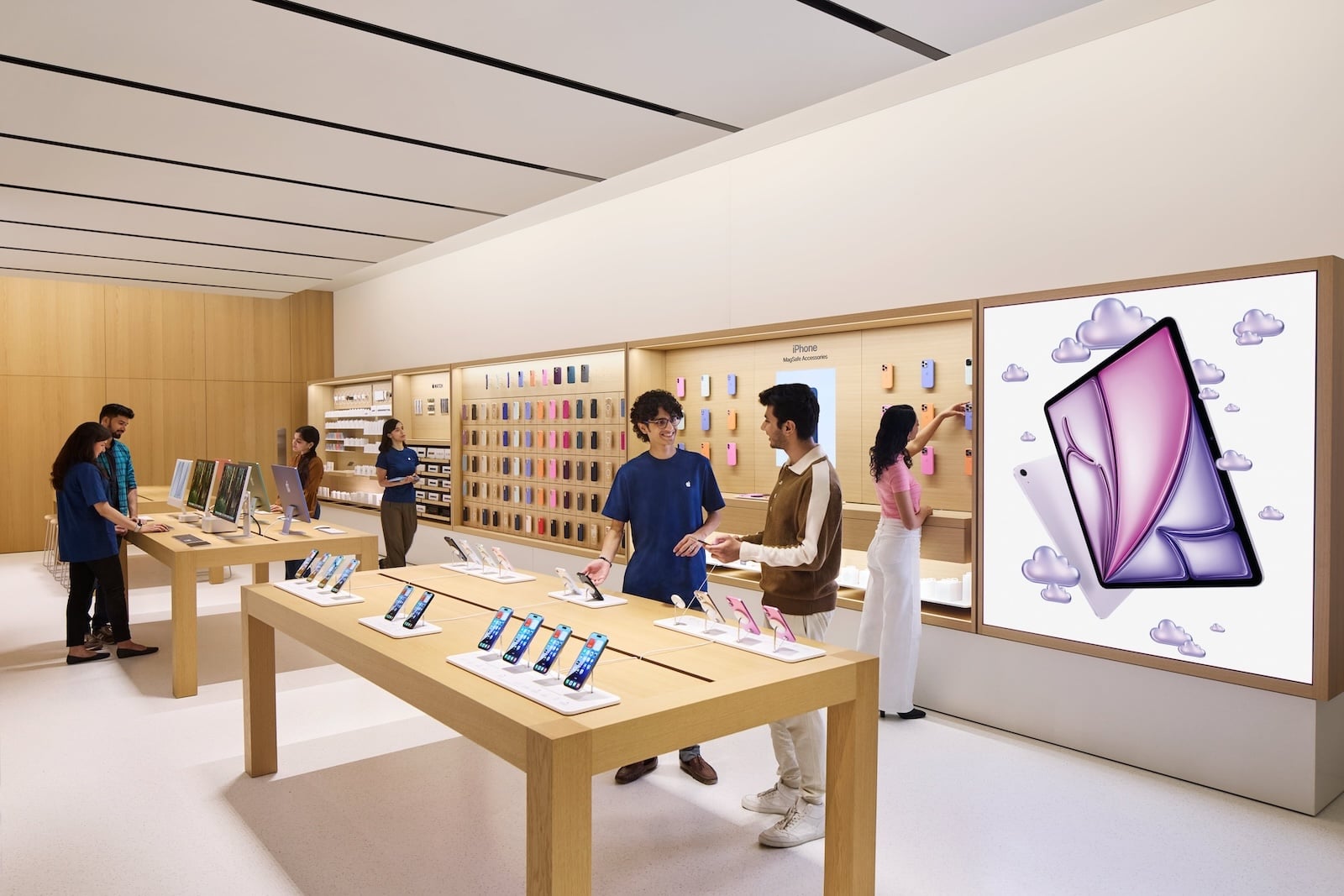 Verkaufsfläche im Apple Store Hebbal mit iPhone-Tisch, MagSafe-Zubehörwand und beratenden Mitarbeitenden, wo Apple seinen Umsatz in Indien erwirtschaftet