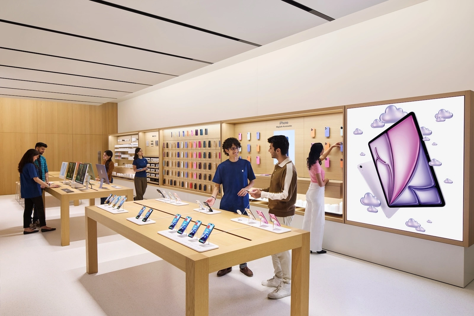 Verkaufsfläche im Apple Store Hebbal mit iPhone-Tisch, MagSafe-Zubehörwand und beratenden Mitarbeitenden, wo Apple seinen Umsatz in Indien erwirtschaftet