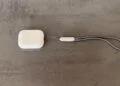 Ladecase der AirPods Pro 3 mit grauer Trageschlaufe auf einer Betonfläche, Modell ohne Kamera