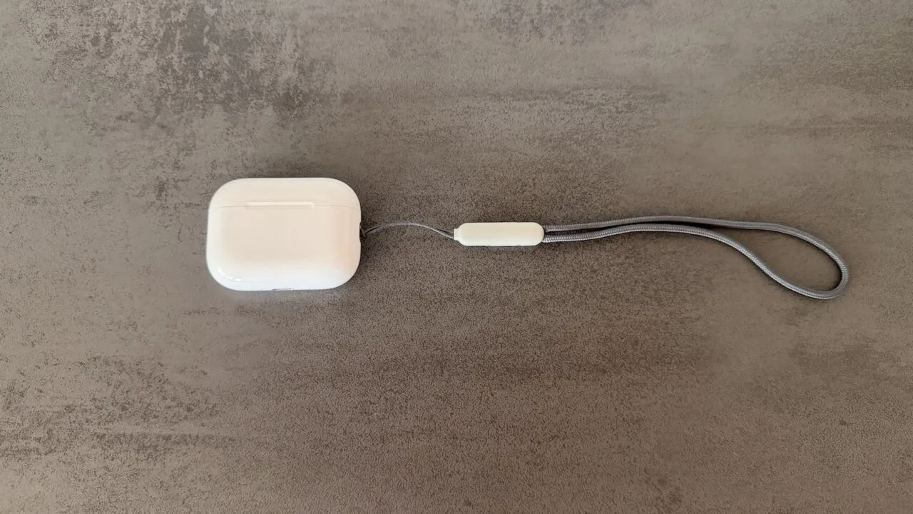 Ladecase der AirPods Pro 3 mit grauer Trageschlaufe auf einer Betonfläche, Modell ohne Kamera