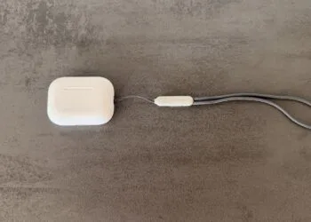 Ladecase der AirPods Pro 3 mit grauer Trageschlaufe auf einer Betonfläche, Modell ohne Kamera