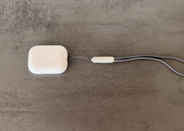 Ladecase der AirPods Pro 3 mit grauer Trageschlaufe auf einer Betonfläche, Modell ohne Kamera