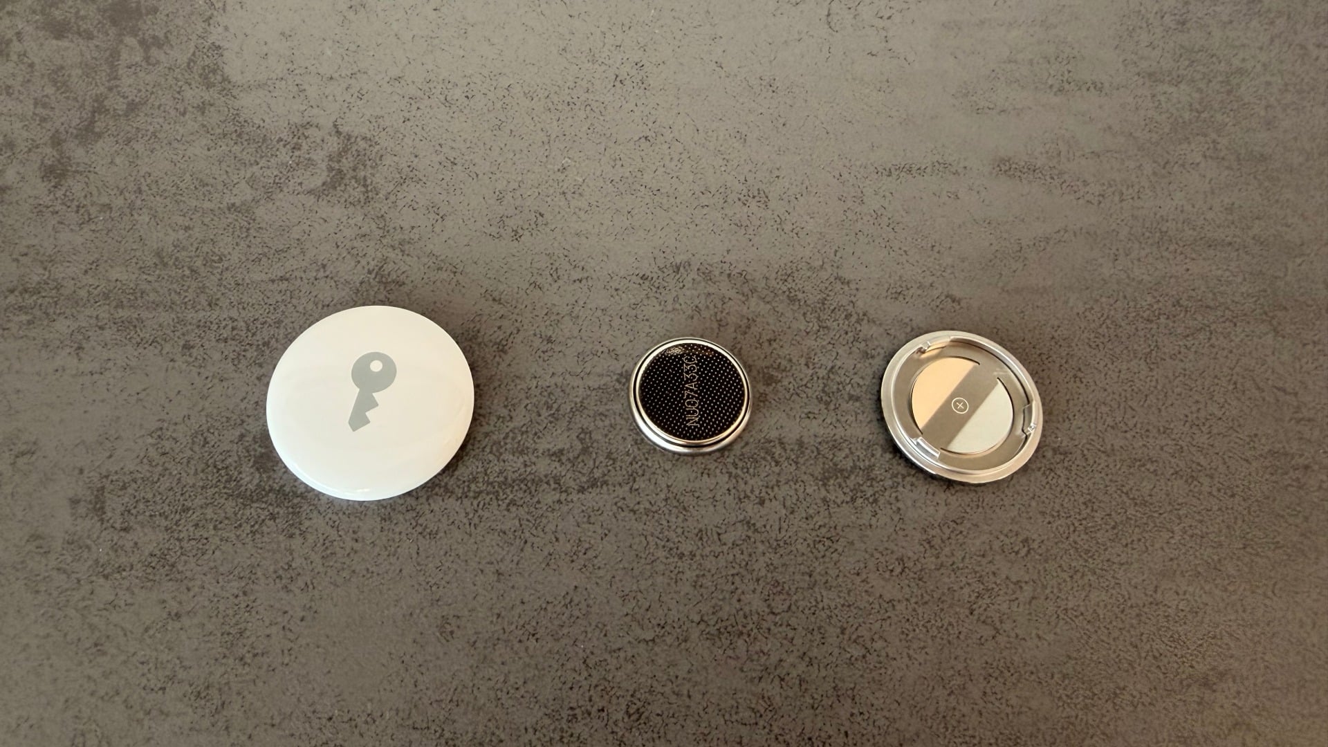 Geöffneter AirTag mit Gehäuse links, Knopfzelle in der Mitte und Abdeckung rechts, das Entnehmen der Batterie beendet AirTag-Stalking sofort
