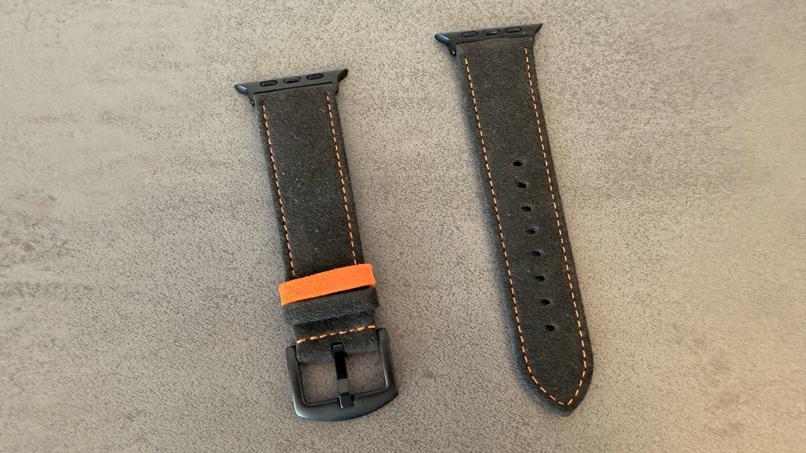 Both halves of the strap from the Alcantara set with orange stitching, a black pin buckle and adjustment holes