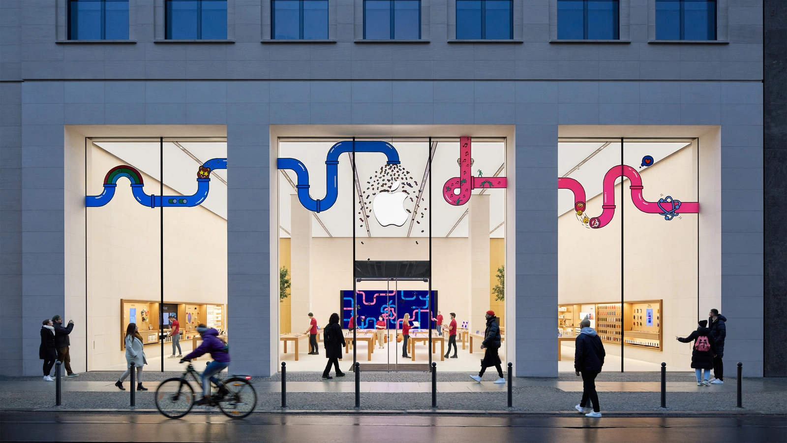 Symbolbild zu Apple Aktie Jefferies: Beleuchteter Apple Store in der Rosenthaler Straße in Berlin am Abend mit Passanten davor