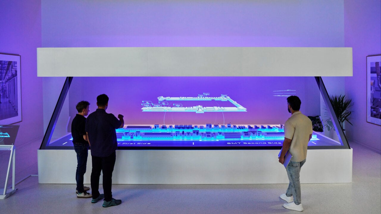 Drei Personen betrachten im Schulungswerk von Apple Houston eine holografische Darstellung einer Fertigungsstraße