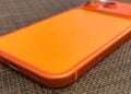 Glass panel set into the aluminium frame on the back of an iPhone 17 Pro Max in Cosmic Orange, whereas the iPhone 20 glass design is said to wrap the glass around the edges