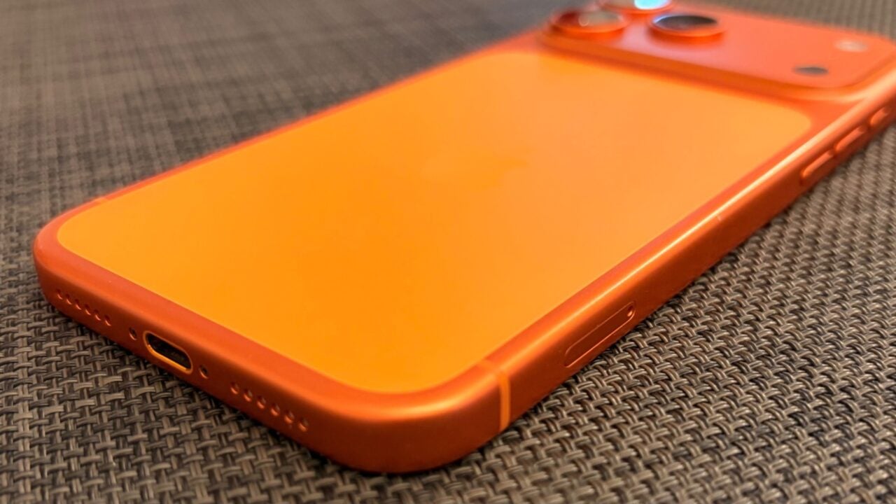 Glass panel set into the aluminium frame on the back of an iPhone 17 Pro Max in Cosmic Orange, whereas the iPhone 20 glass design is said to wrap the glass around the edges