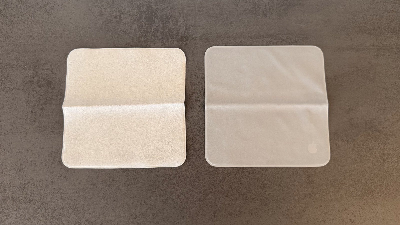 Two Apple polishing cloths side by side on a grey background, on the left the 2021 version in warm beige, on the right the 2026 version in a cooler grey tone.