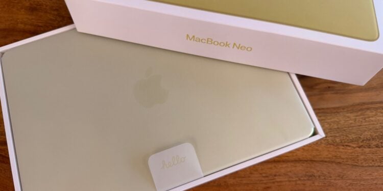 Half-opened box of the MacBook Neo in Citrus, the device still resting in its protective sleeve inside the packaging