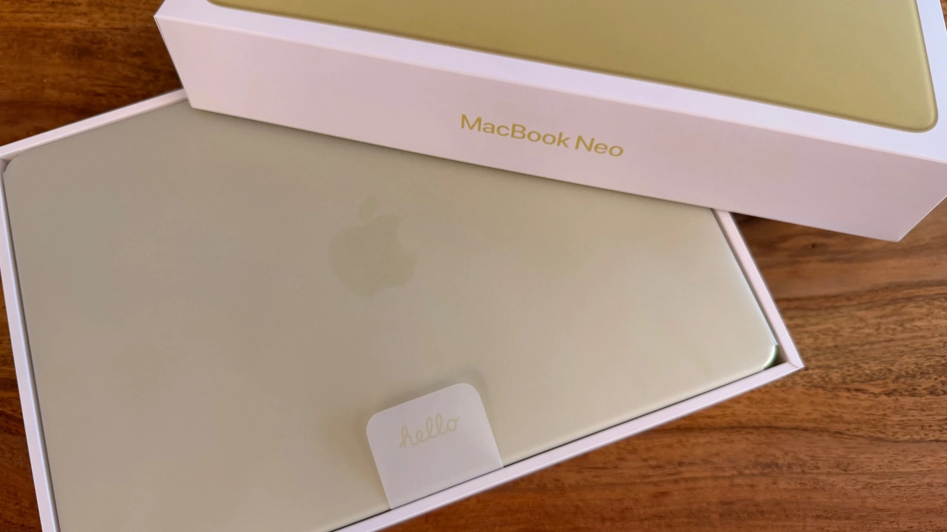 Halb geöffnete Verpackung des MacBook Neo in Citrus, das Gerät liegt noch in der Schutzhülle im Karton