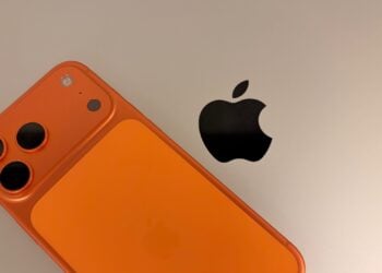 iPhone 17 Pro Max in Cosmic Orange auf einem silbernen MacBook Pro neben dem Apple-Logo – die beiden Geräte, um deren Absicherung es beim iPhone auf Reisen geht