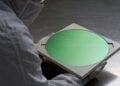 Worker in a cleanroom suit holding a semiconductor wafer of the kind TSMC also produces for iPhone 18 Pro chips