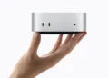 Mac mini M6 in Silber wird von einer Hand gehalten, Vorderseite mit zwei USB-C-Anschlüssen sichtbar