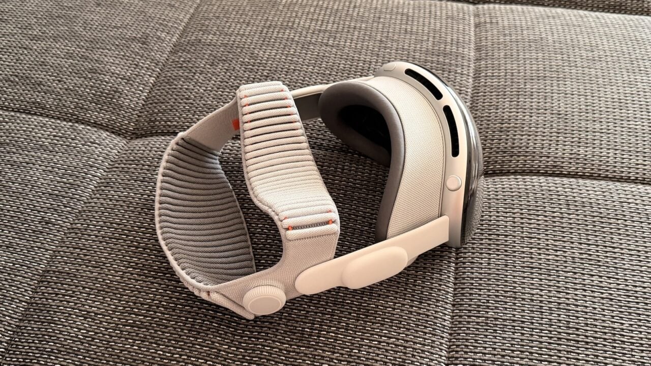 Apple Vision Pro mit hellem Dual Knit Band liegt seitlich auf einer grau melierten Sofafläche
