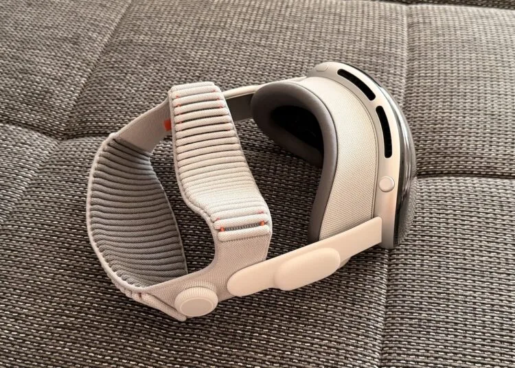 Apple Vision Pro mit hellem Dual Knit Band liegt seitlich auf einer grau melierten Sofafläche