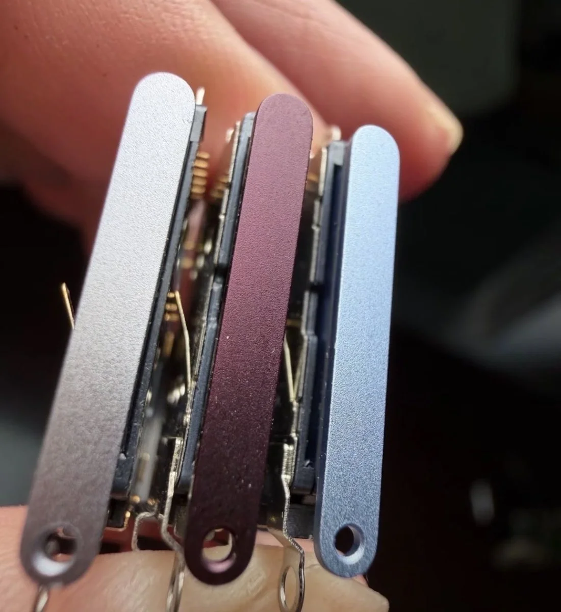 Drei SIM-Kartenschlitten in Silber, Dark Cherry und Hellblau als Hinweis auf die iPhone 18 Pro Farben