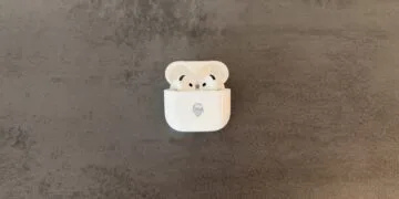 AirPods 5 im geöffneten Ladecase mit Memoji-Gravur auf grauem Steinuntergrund