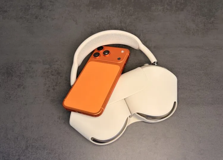 AirPods-Equalizer einstellen: orangefarbenes iPhone auf AirPods Max in der Hülle auf grauem Untergrund
