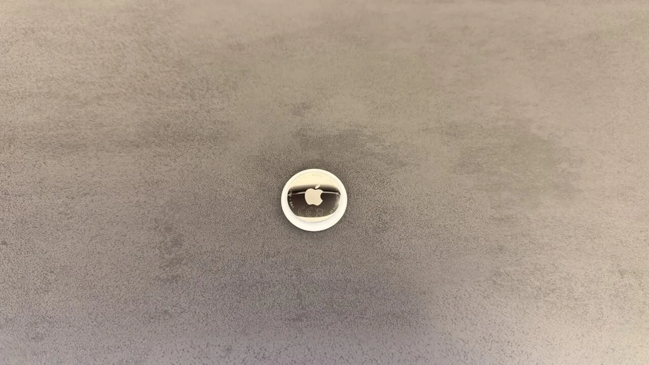Apple KI-Pin: ein AirTag als Größenvergleich auf grauer Fläche