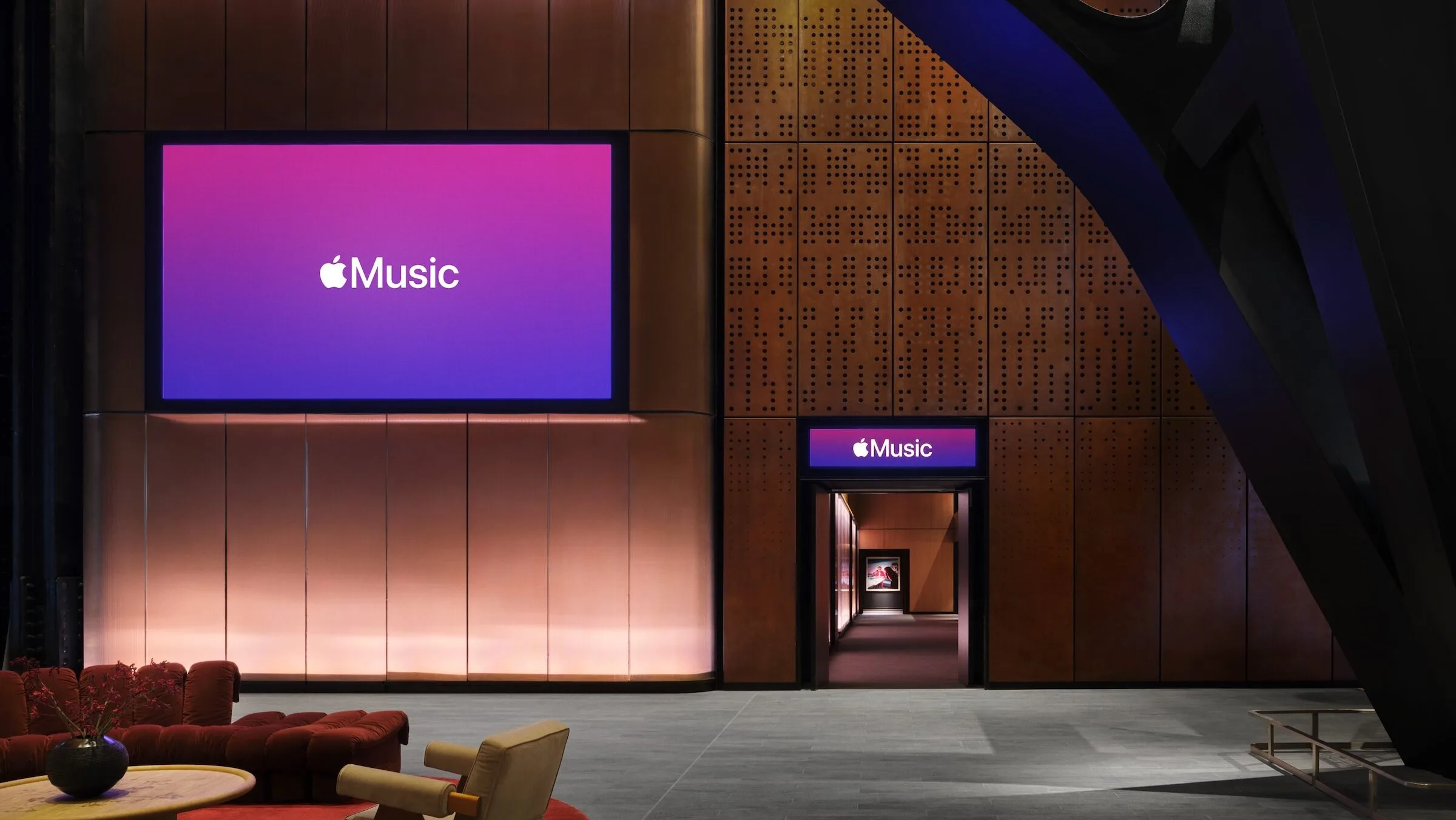 Foyer der Apple Music Hall mit großem Apple-Music-Bildschirm, Eingang mit Leuchtschild und Sitzecke im Vordergrund