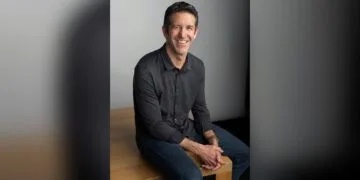 Thanksgiving-Woche bei Apple frei: CEO John Ternus in dunklem Hemd sitzt lächelnd auf einem Holztisch
