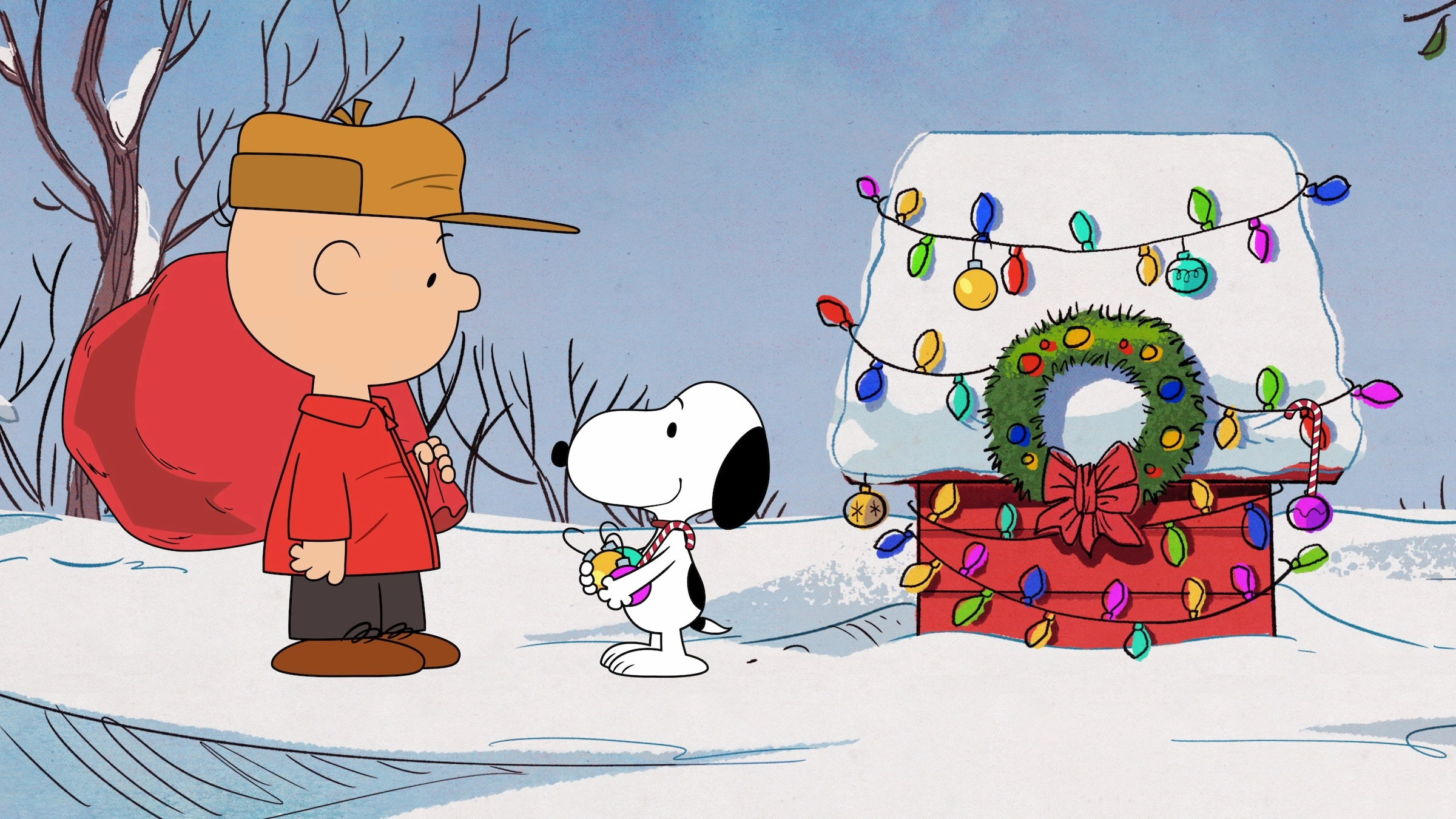 Charlie Brown mit rotem Sack und Snoopy mit Christbaumkugeln vor der geschmückten Hundehütte, Szene aus einem Peanuts-Weihnachtsspecial bei Apple TV