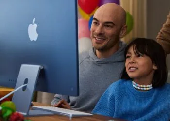 Ein Kind sitzt mit einem Erwachsenen vor einem blauen iMac, Motiv zu Apples Leitfaden für Bildschirmzeit in Familien