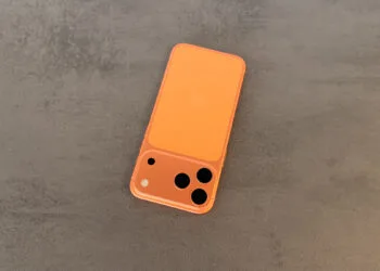 Orangefarbenes iPhone mit Dreifachkamera liegt auf grauem Stein, Symbol für die gestiegene iPhone Produktion