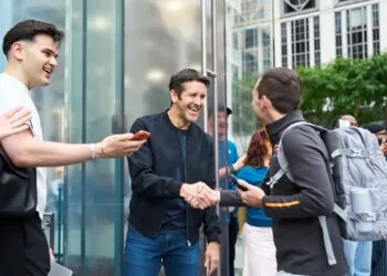 John Ternus begrüßt vor dem Apple Store Fifth Avenue in New York einen Kunden per Handschlag, umringt von applaudierenden Mitarbeitern