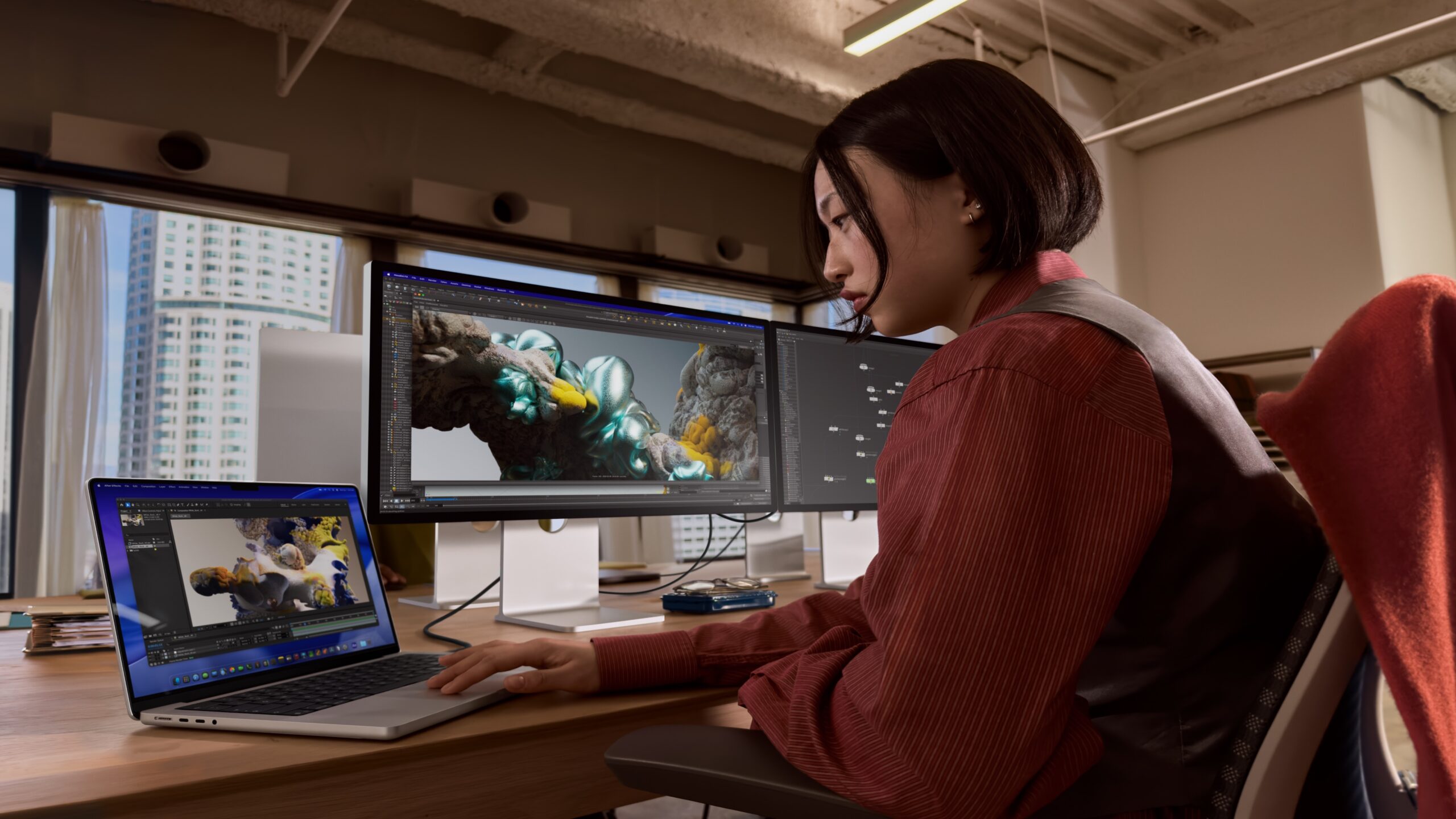 Mac buying guide: woman working on a silver MacBook Pro next to two external displays showing 3D software