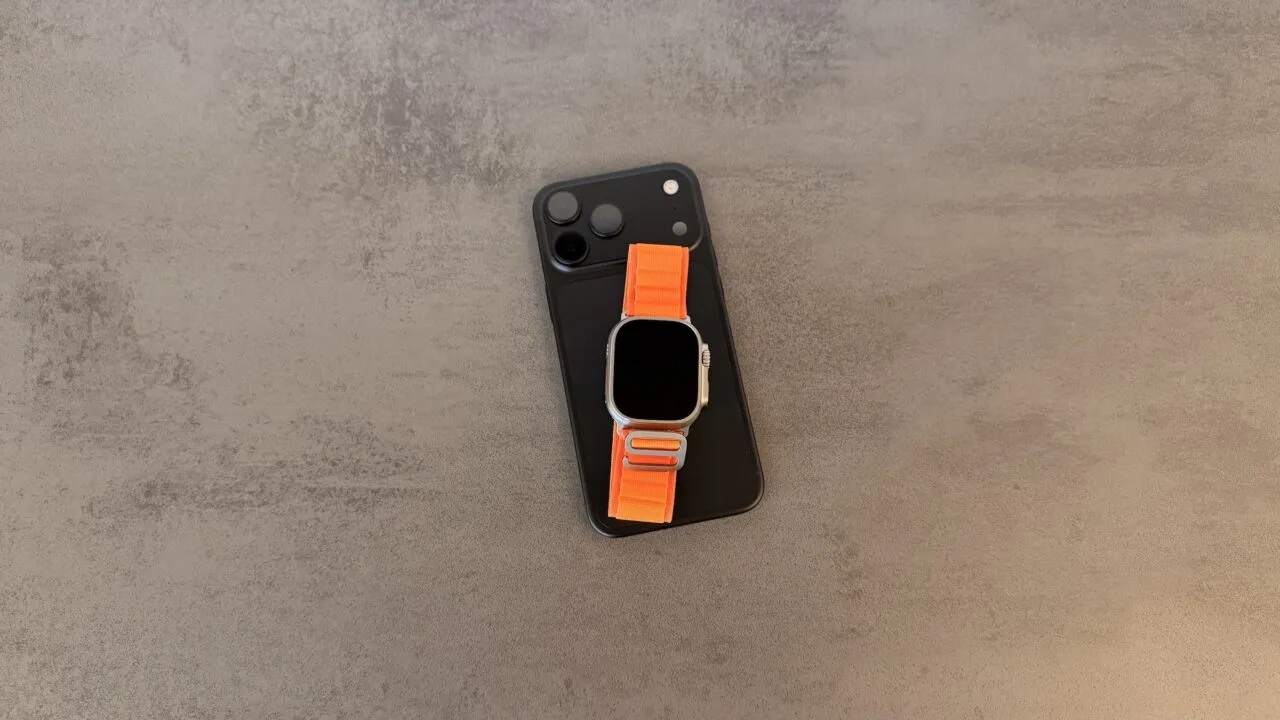 Taptic Engine in iPhone und Apple Watch: schwarzes iPhone mit Dreifachkamera, darauf eine Apple Watch Ultra mit orangefarbenem Alpine Loop