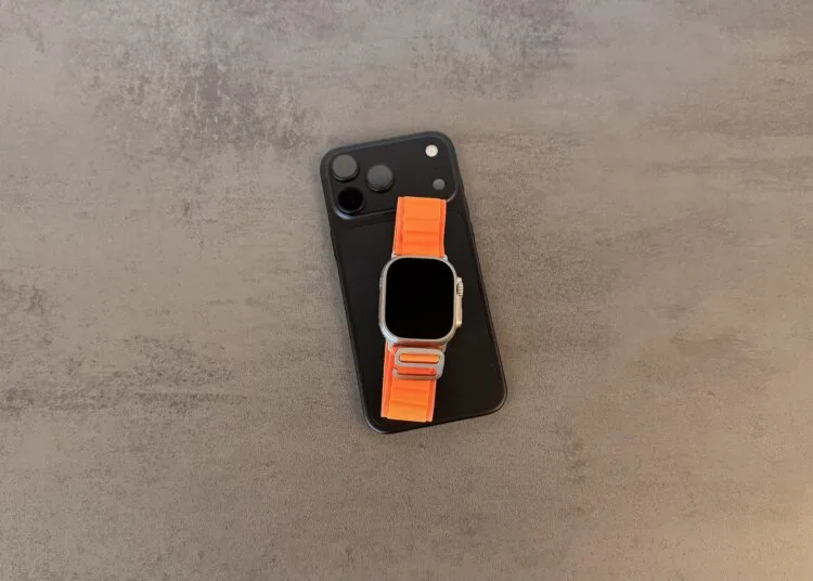 Taptic Engine Urteil: schwarzes iPhone mit Dreifachkamera, darauf eine Apple Watch Ultra mit orangefarbenem Alpine Loop