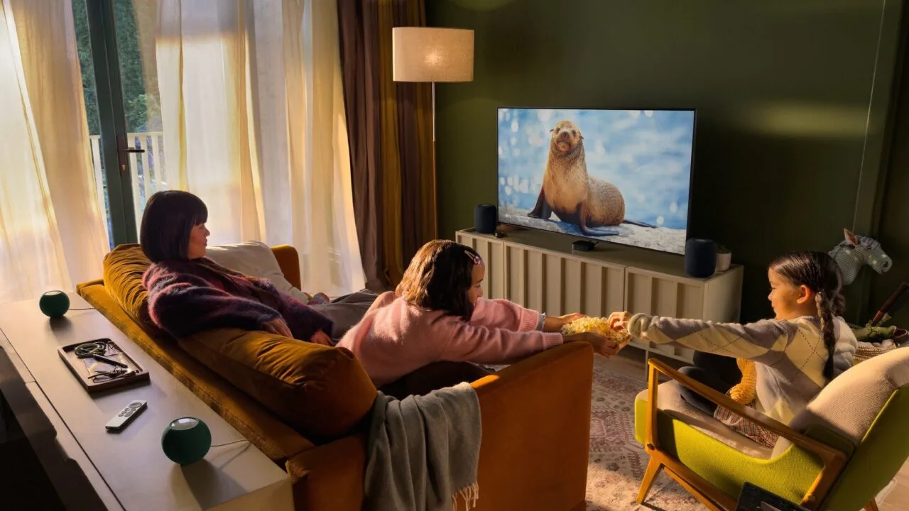 Apple Event Welcome home: Familie im Wohnzimmer vor einem Fernseher mit Apple TV, daneben zwei HomePod und hinter dem Sofa zwei grüne HomePod mini