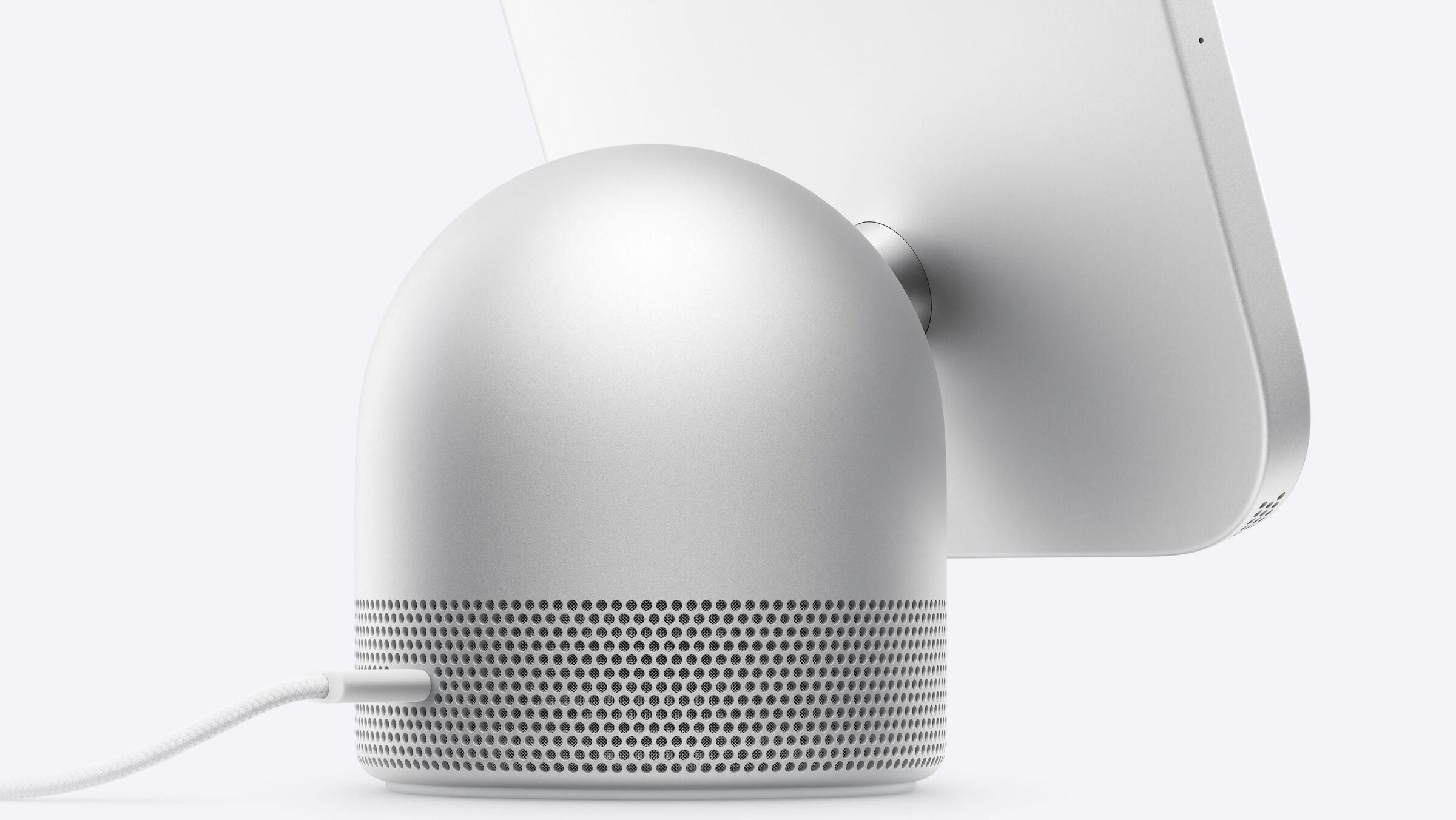 Domed speaker base of Apple HomeView with speaker grille and connected USB-C cable, with the back of the display behind it