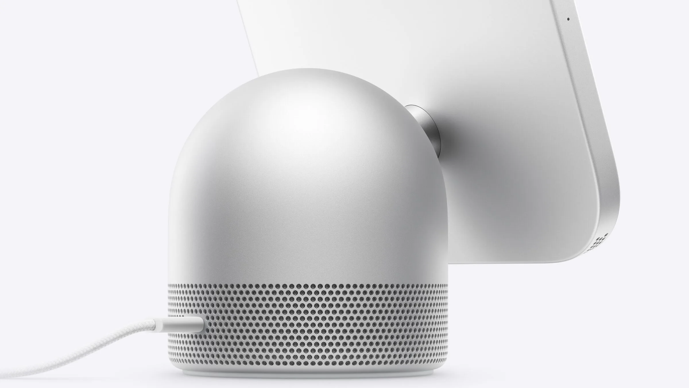 Gewölbter Lautsprecherfuß von Apple HomeView mit Lautsprechergitter und angeschlossenem USB-C-Kabel, dahinter die Rückseite des Displays