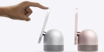 HomeView Roboterarm: Eine Hand neigt mit einem Finger das Display einer silbernen HomeView, daneben steht ein zweites Modell in Rosa