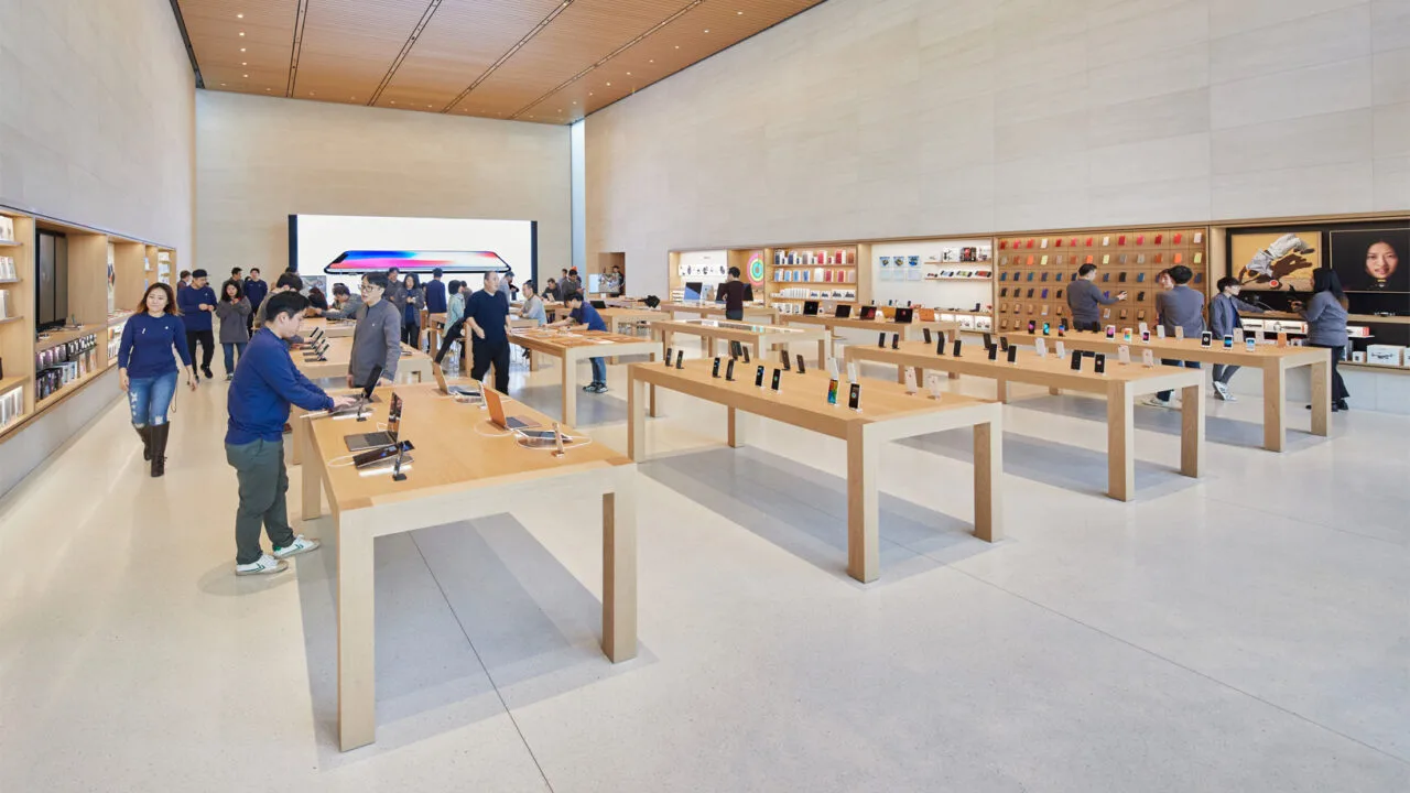 Verkaufsraum eines Apple Store mit Holztischen, ausgestellten iPhones und Mitarbeitern, an denen die iPhone Rückgabe im Apple Store abgewickelt wird