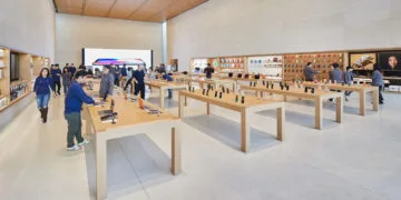 Verkaufsraum eines Apple Store mit Holztischen, ausgestellten iPhones und Mitarbeitern, an denen die iPhone Rückgabe im Apple Store abgewickelt wird